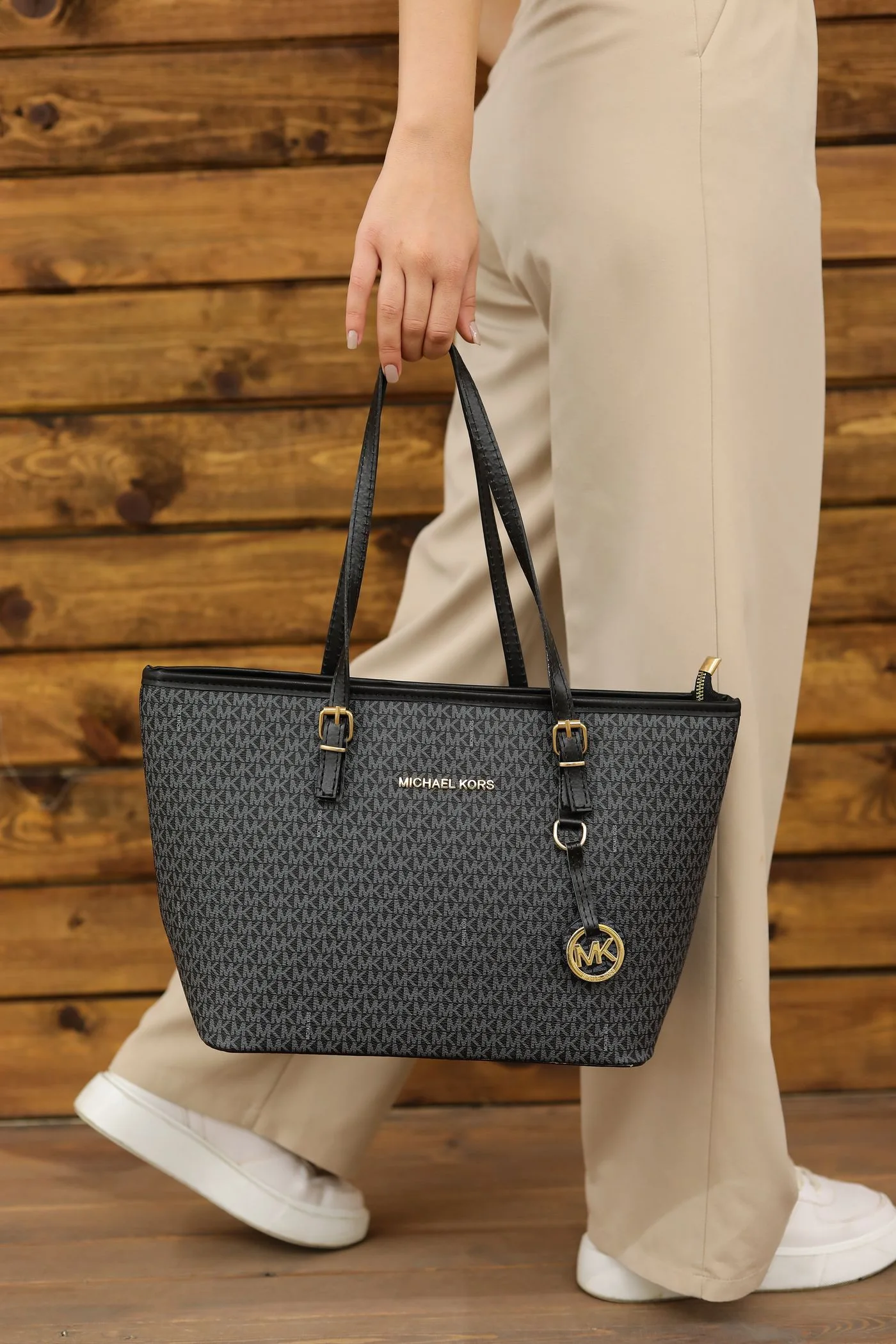 A woman holding a black tote bag against a wooden backdrop.