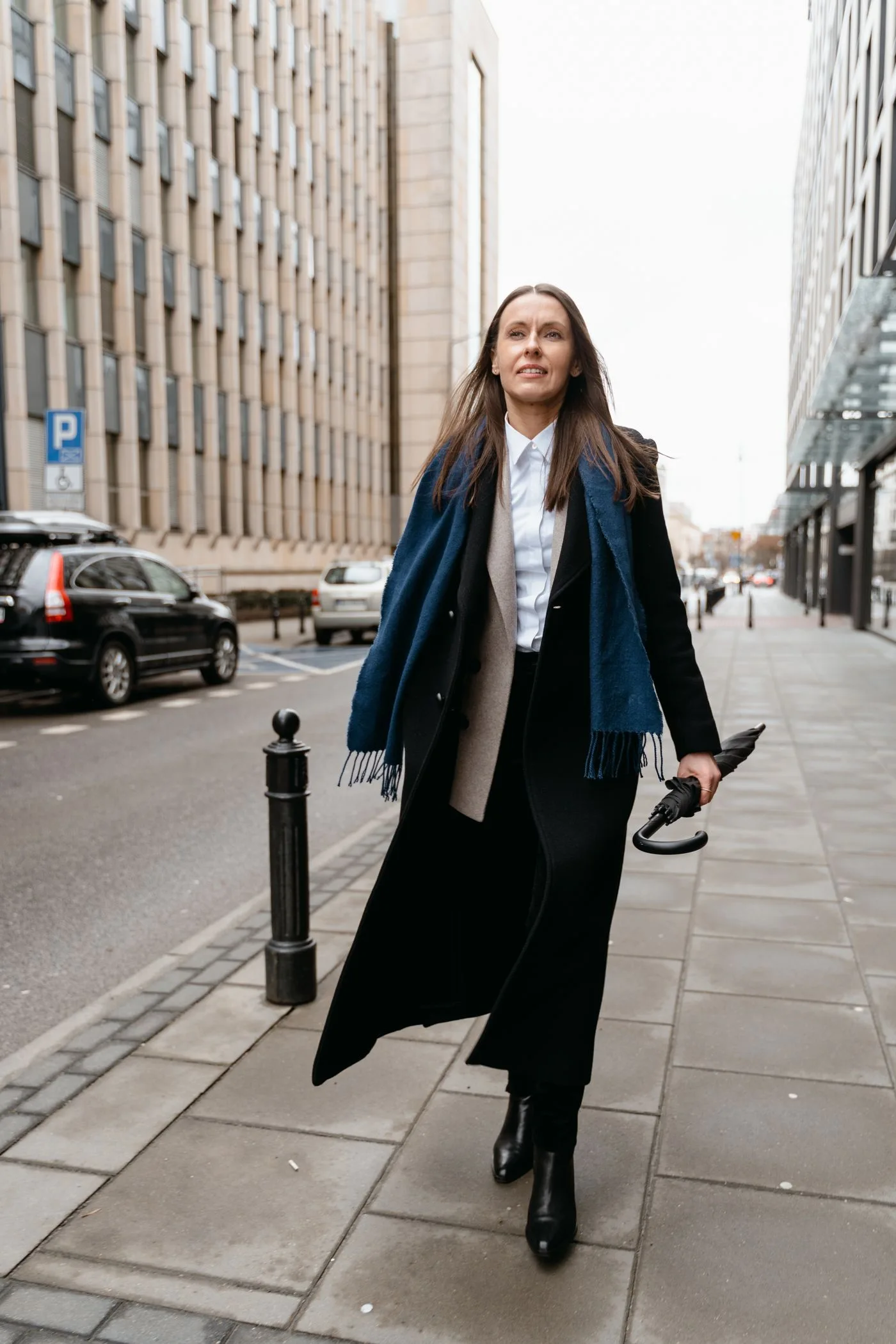 A person in a black coat and boots on a city sidewalk.